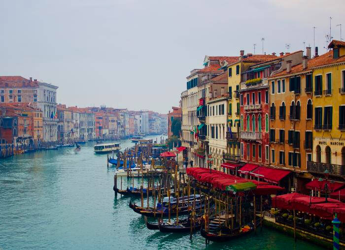 Colored photograph of brightly colored buildings lining a river. Boats docked and in the water.